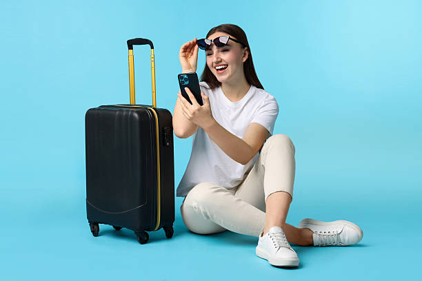 istock Woman with suitcase and smartphone on light blue background 2233344703