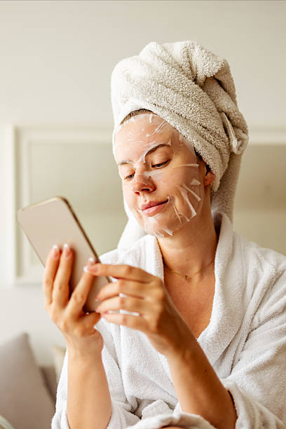 istock Woman Wearing Face Mask Relaxing With Towel and Robe While Browsing Phone 2233350978