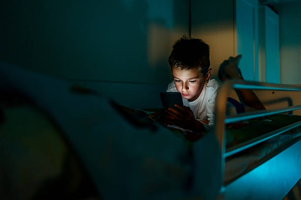 istock Young Boy Using Tablet on Bed in Dimly Lit Room at Night 2233351000