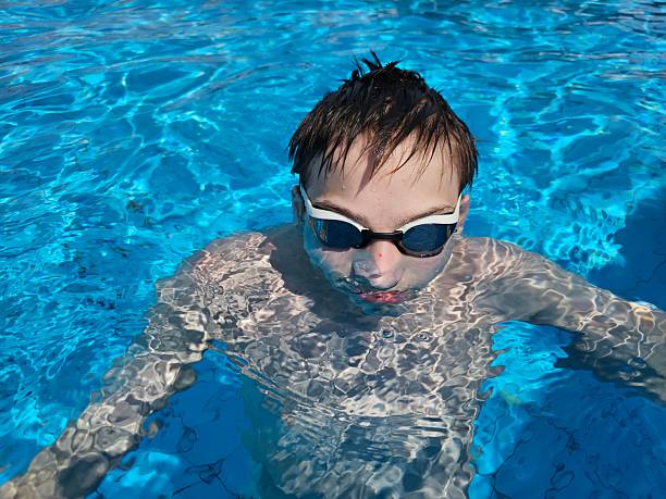 Young boy swimming in clear blue pool wearing goggles on a sunny day