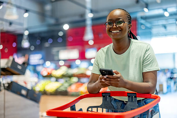 istock Smiling Woman Grocery Shopping While Using Phone at a Market 2233353166