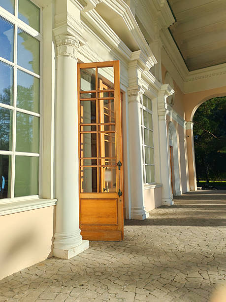 A neoclassical building with tall white columns and an open wooden door framed by large windows. The interplay of sunlight and shadow highlights the elegance of classical architecture.