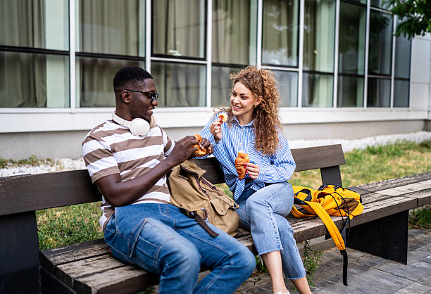 istock Smiling students eating croissants on bench outside university 2233364044