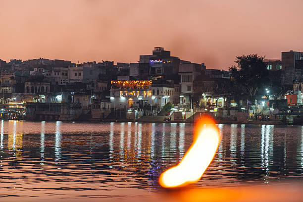 Evening view of a lakeside cityscape with a glowing flame in the forefront, showcasing serene reflections and the enchanting ambiance of the location.