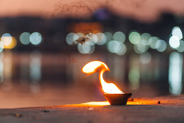 A glowing oil lamp captured against a softly focused background of vibrant lights, reflecting spiritual and tranquil feelings. It evokes a sense of peace and cultural tradition in India.