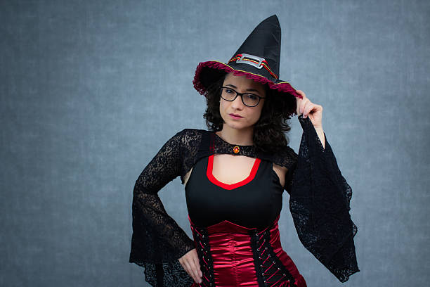istock Charming witch, with curly hair, wearing eyeglasses, touching her witch's hat with one hand. 2233372998