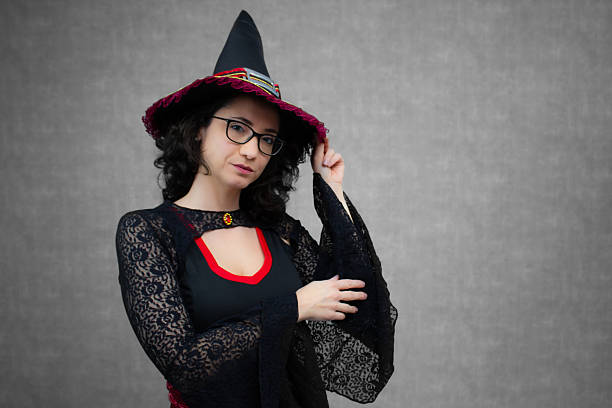 istock Charming witch, with curly hair, wearing eyeglasses, touching her witch's hat with one hand. 2233372999
