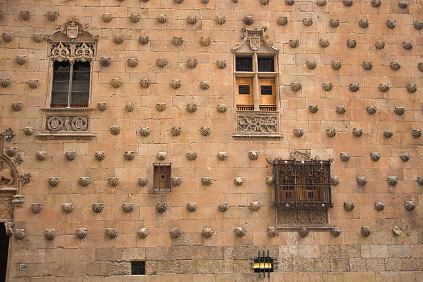 Facade with shells at Casa de las Conchas: Historic sandstone wall with scallop shells and ornate window grille in Salamanca's famous Casa de las Conchas, Spain.