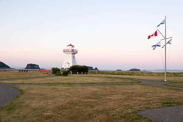 Flapping in the wind, flags and a lighthouse stand at the high point overlooking the sea stacks of Five Island Provincial Park, Nova Scotia, Canada.