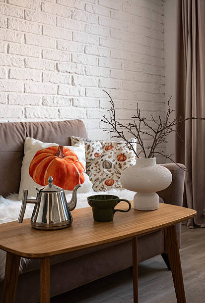 istock A living room that showcases a cozy sofa along with beautiful natural autumn decor elements and accents: teapot, glass, ceramic vase with dry flowers and branches, pillows with autumn pumpkins decor. 2233378058