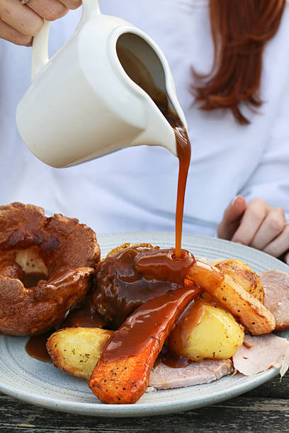Stock photo shows a hearty roast dinner featuring sliced chicken, Yorkshire pudding, roasted potatoes, carrots, broccoli, and stuffing, with rich gravy being poured over the plate. Perfect for a traditional family meal, this nutritious comfort food combines protein and vegetables