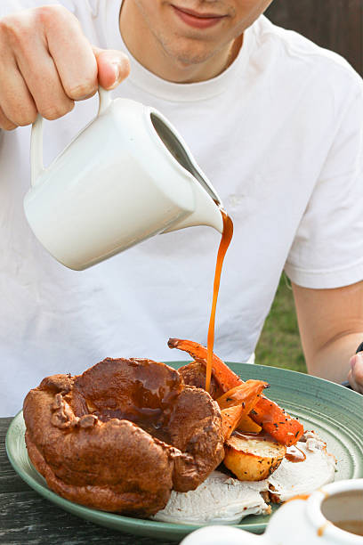 istock Image of eating roast dinner, sliced chicken, yorkshire pudding, potatoes, carrots, broccoli, stuffing, pouring gravy, family meal 2233379837