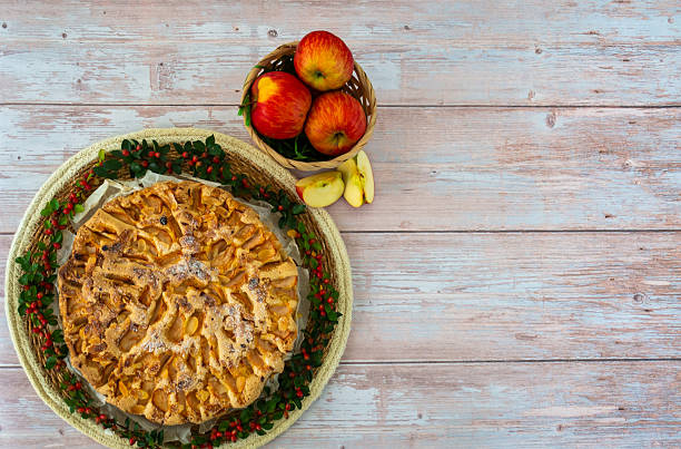 A pie with apples on top of it. The pie is surrounded by a wicker basket with apples