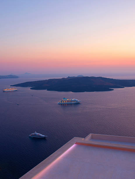 Greece,  Santorini, ferries in aegean sea at anchor, table and chairs on patio, sunset.