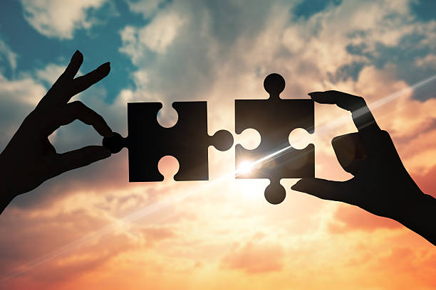 istock Two hands trying to connect puzzle pieces with sunset background 2233391354