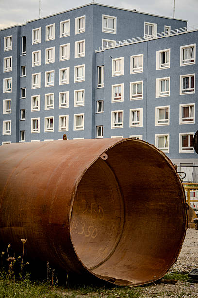 istock Large Rusty Metal Pipe Section Placed On Construction Site Ground: Industrial Infrastructure Component With Urban Background And Safety Barriers 2233392951