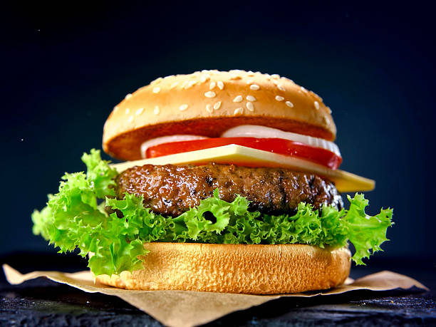 istock hamburger making process macro shot on dark background, beef patty, slices of tomato, cheese, salad turns to a product 2233395144