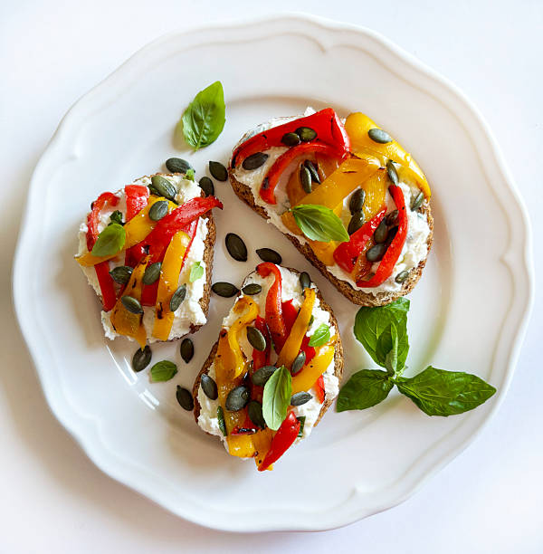 Tasty sandwiches or toasts with grilled peppers, cream cheese, sunflower seeds, olive oil and basil leaves on a white background. Healthy and vegetarian dish. Directly above.