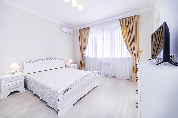 istock A bedroom with a white bed, a television, and a window with curtains 2233424713