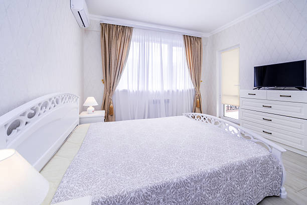 istock A bedroom with a white bed, a television, and a window with curtains 2233425493