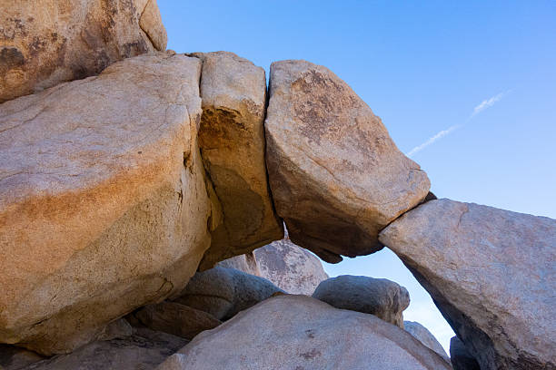 A majestic natural archway, formed by massive, weathered granite boulders, is framed against a brilliant blue sky, showcasing the unique geological beauty of the Joshua Tree National Park landscape