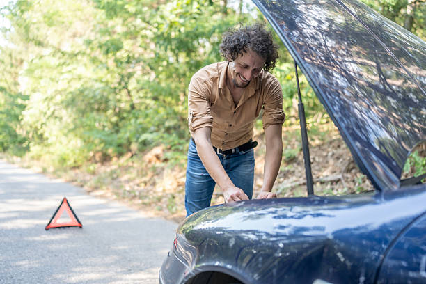 istock Man Repairing Broken Car on Rural Road with Warning Triangle Displayed 2233430438