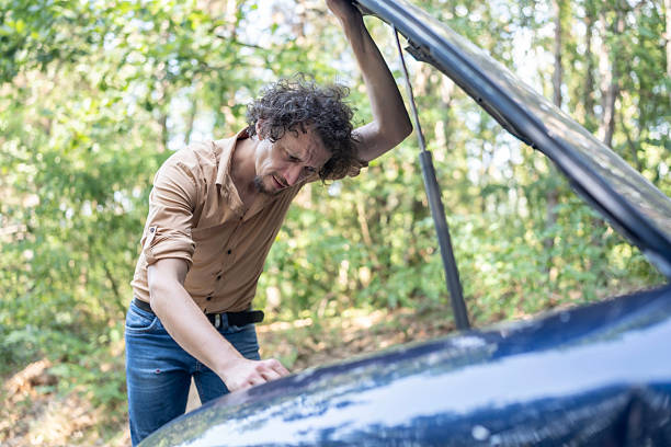 istock Concerned Man Checking Under a Car Hood Outdoors on a Sunny Day 2233430446