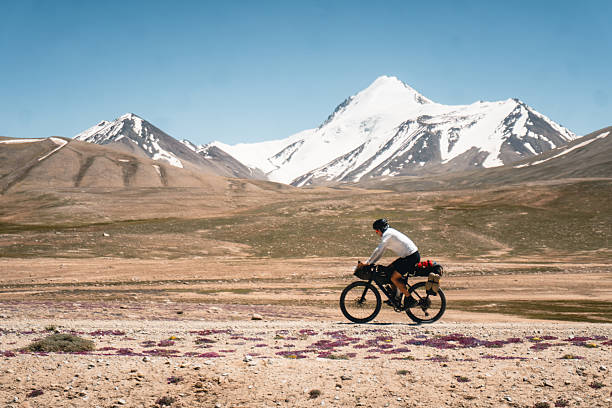 Bikepacker rides remote road below snowcapped mountains, Pamir highway