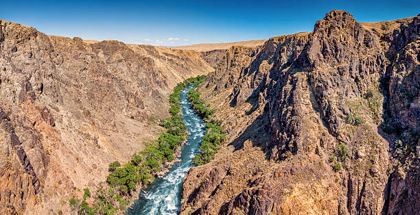 istock Dramatic river canyon with steep rocky cliffs and fast flowing water surrounded by sparse desert vegetation under clear blue sky 2233439458