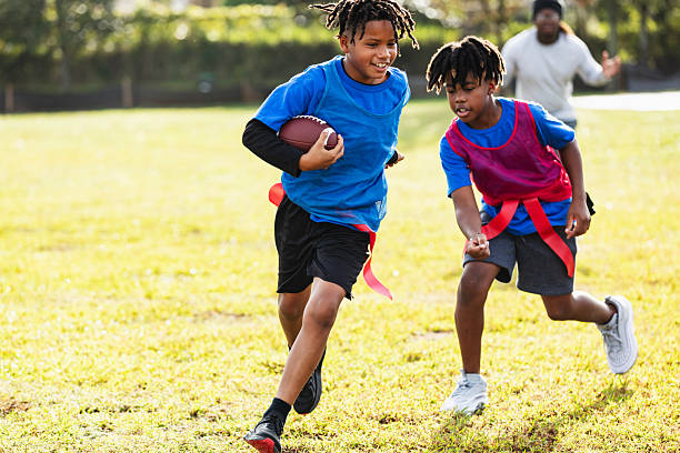 Two boys playing flag football. A 10 year old Hispanic boys is running with the ball tucked under his arm. The opponent, a 9 year old multiracial boy, is chasing him.