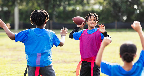 A 10 year old Hispanic boy in the park playing flag football. He is holding the ball, getting ready to pass it over his opponents.