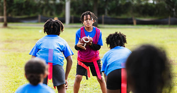 A 10 year old Hispanic boy in the park playing flag football. He is holding the ball, getting ready to pass it over his opponents.
