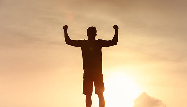 istock Man silhouette stands with arms raised, triumph and freedom 2233441971