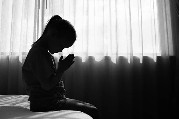 Little child praying while sitting on bed.