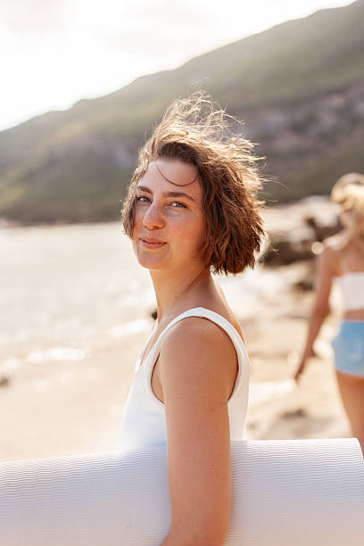 istock Young woman holding surfboard and looking at camera on beach 2233444084