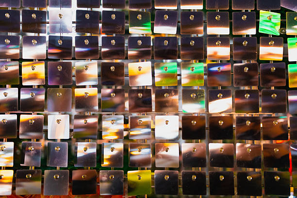 Close-up of shiny square sequins reflecting colorful christmas lights, creating a festive and vibrant background