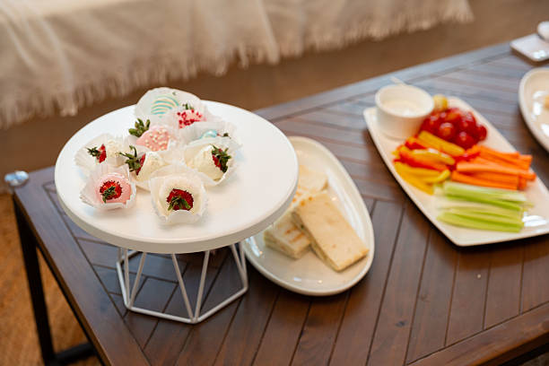 A beautifully arranged table features decorative desserts on a white stand and a colorful assortment of vegetables and dips on a wooden surface, perfect for gatherings.