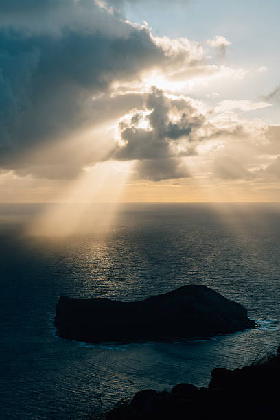 istock Rays of sunshine beaming through clouds above rocky island 2233448417