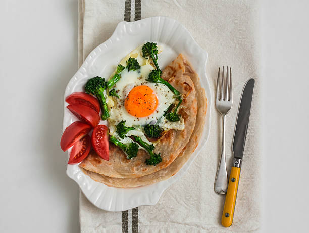 Delicious breakfast, brunch - roti tortilla, fresh tomatoes, fried egg with broccoli on a light background, top view