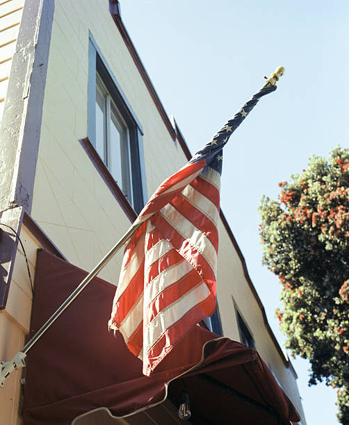 An American Flag hangs from the front porch of a home. A row of houses directs your eye to a Church at the end of the street symbolizing Religion in America.
