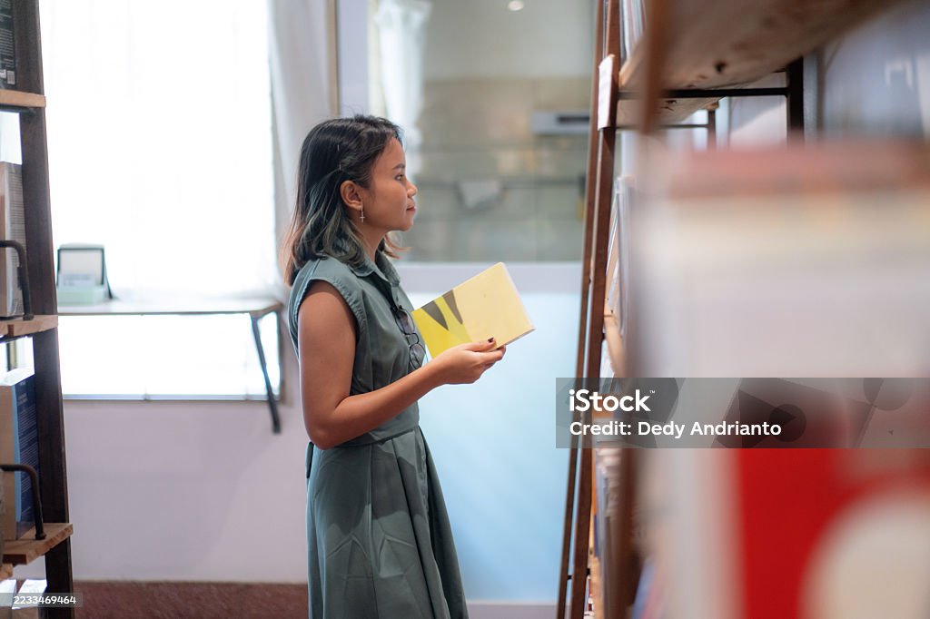 Close Up of Young Southeast Asian Woman Browsing Independent Books Store A young woman in a green dress browses through a collection of art and design books displayed on wooden shelves inside a cozy independent bookstore in Bandung. The setting is calm and softly lit, evoking a sense of curiosity and appreciation for literature and visual culture. Natural daylight filters in through the window, enhancing the warm, contemplative atmosphere. 20-29 Years Stock Photo Close Up of Young Southeast Asian Woman Browsing Independent Books Store A young woman in a green dress browses through a collection of art and design books displayed on wooden shelves inside a cozy independent bookstore in Bandung. The setting is calm and softly lit, evoking a sense of curiosity and appreciation for literature and visual culture. Natural daylight filters in through the window, enhancing the warm, contemplative atmosphere. 20-29 Years Stock Photo