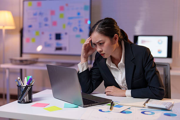 istock Young stressed businesswoman having headache while using laptop and working with financial documents sitting at desk in office late at night 2233474183