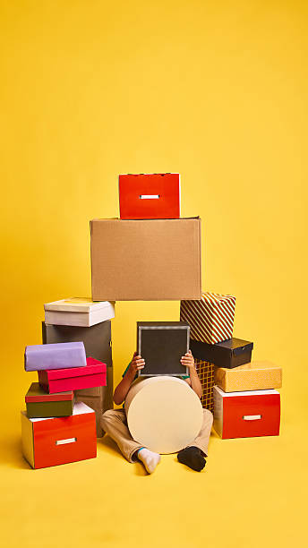 istock Playful child hiding behind gift boxes on bright yellow background 2233474425
