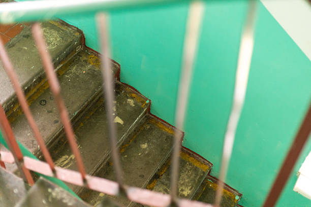 The worn staircase shows peeling paint, rust, and a shabby railing, indicative of an old building's decay. The vibrant green wall contrasts with the staircase's poor state, highlighting neglect.