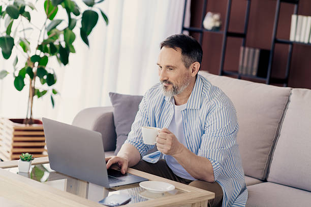 istock Mature professional working on laptop while relaxing at home with coffee in a contemporary and cozy living space. 2233477470