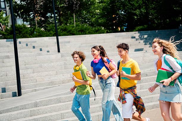 istock Group of cheerful students walking together outdoors on a sunny day while carrying book and enjoying friendship 2233477926