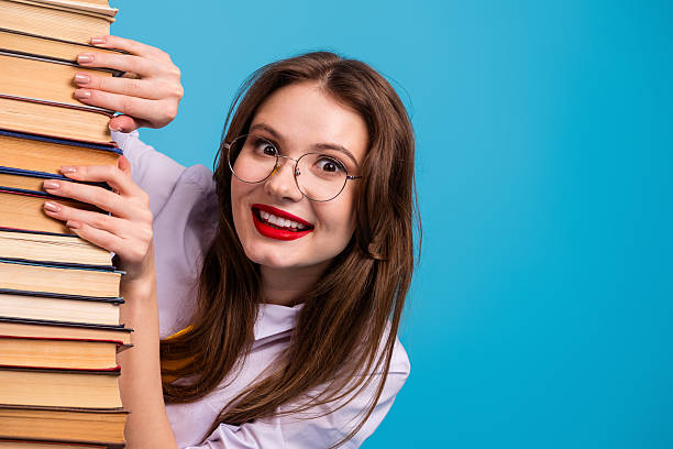 istock Young woman in glasses smiling while leaning on a stack of book against a vibrant blue background 2233478363
