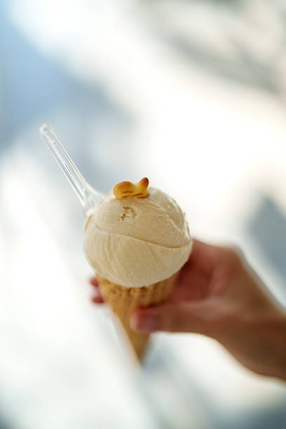 Close-up of a hand holding a ice cream cone with a small clear spoon, captured in soft natural light with copy space.