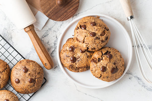 istock Fresh chocolate American chip cookies with nuts and chocolate drops on white marble background. Flat lay of cookies with stylish cutlery and pastry chef accessories. Recipe of homemade cookies concept 2233487814