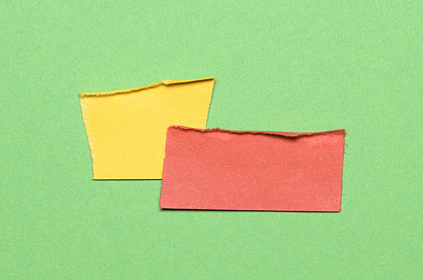 Two yellow red overlapping torn ripped blank paper notes with folded edge dog-ear earmark and copy space for text on green background